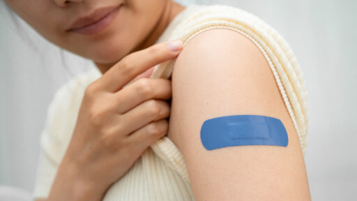A woman looks at her arm which has an adhesive bandage on it following a vaccine shot.